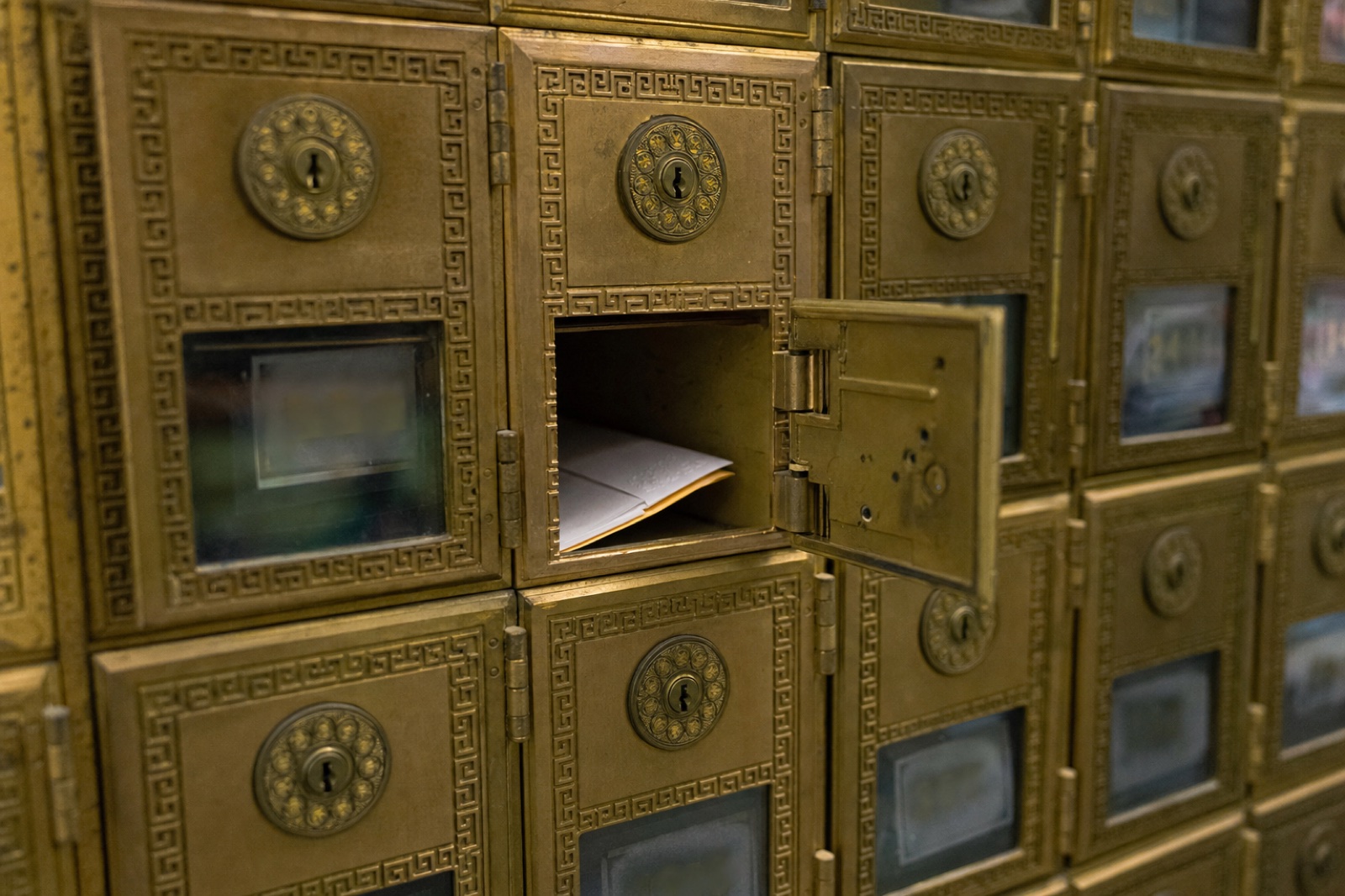 An open brass PO box with mail inside, in a wall of post office boxes.